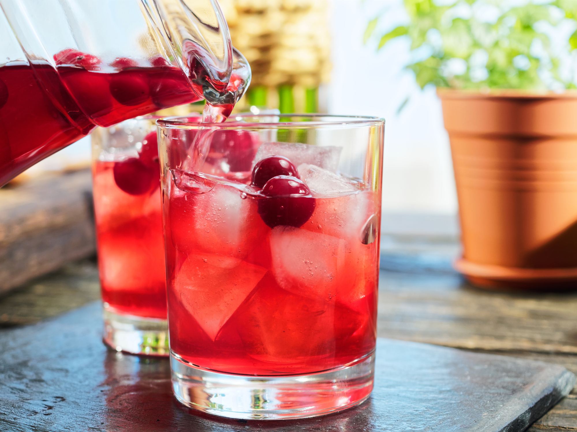 Preparing red sangria with homemade wine, red and green apples, oranges, cranberries and grapes. Pouring sangria into drinking glasses full of ice