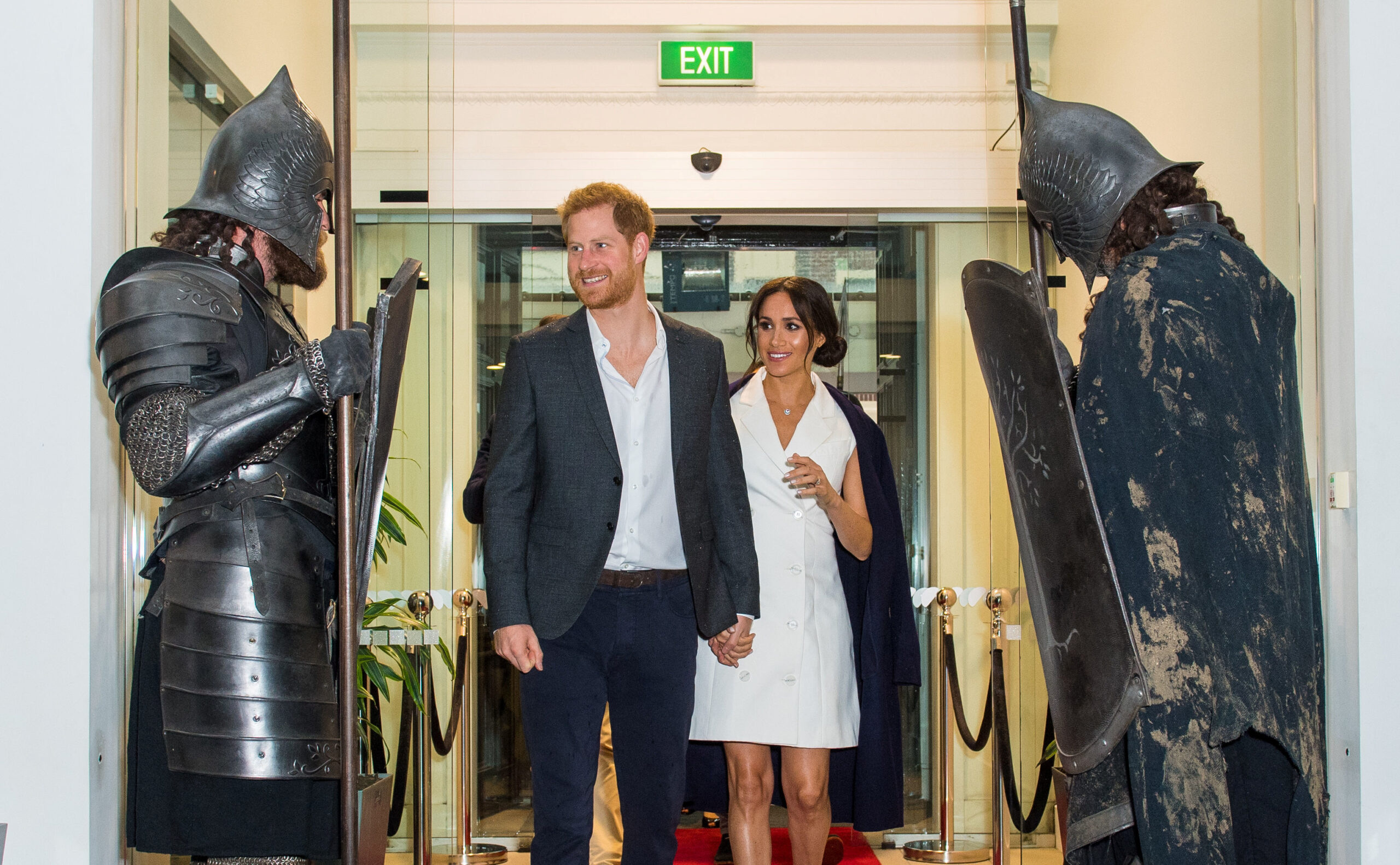 Britain's Prince Harry and Meghan, the Duke and Duchess of Sussex, are greeted by actors in costume as they arrive for a visit to Courtenay Creative, in Wellington