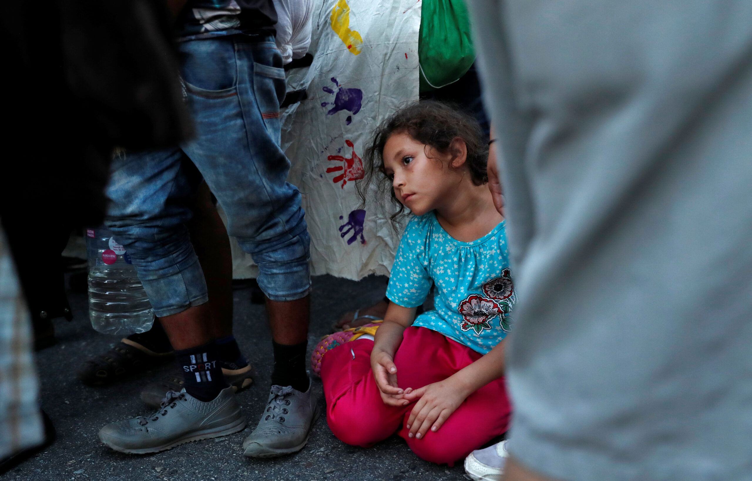 A young girl sits down in the road as her fellow migrants stop for a moment while walking north on their journey to the U.S., from near Huixtla
