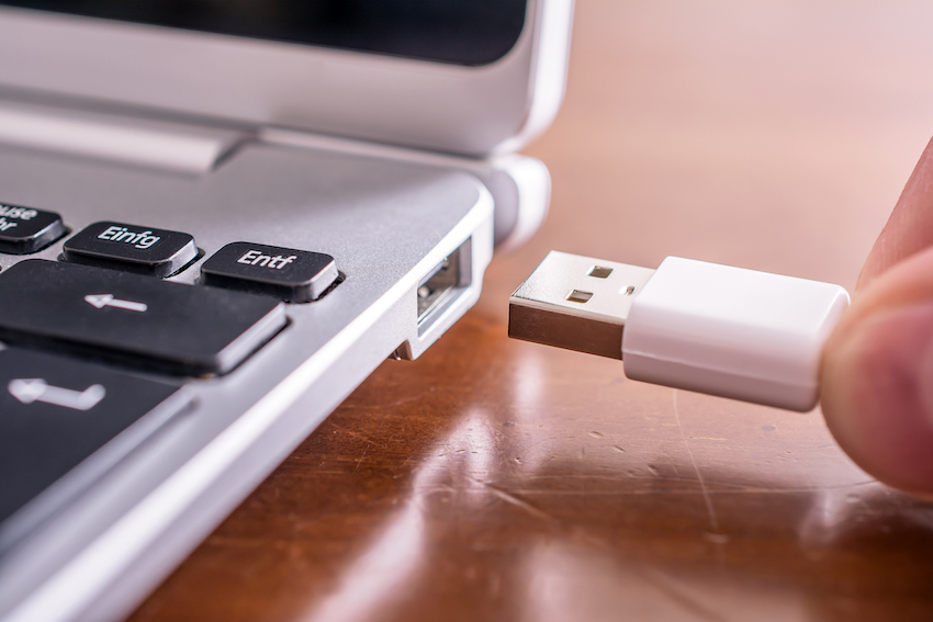 Male Hand Connecting A White USB Cable To The USB Port Of A Small Notebook