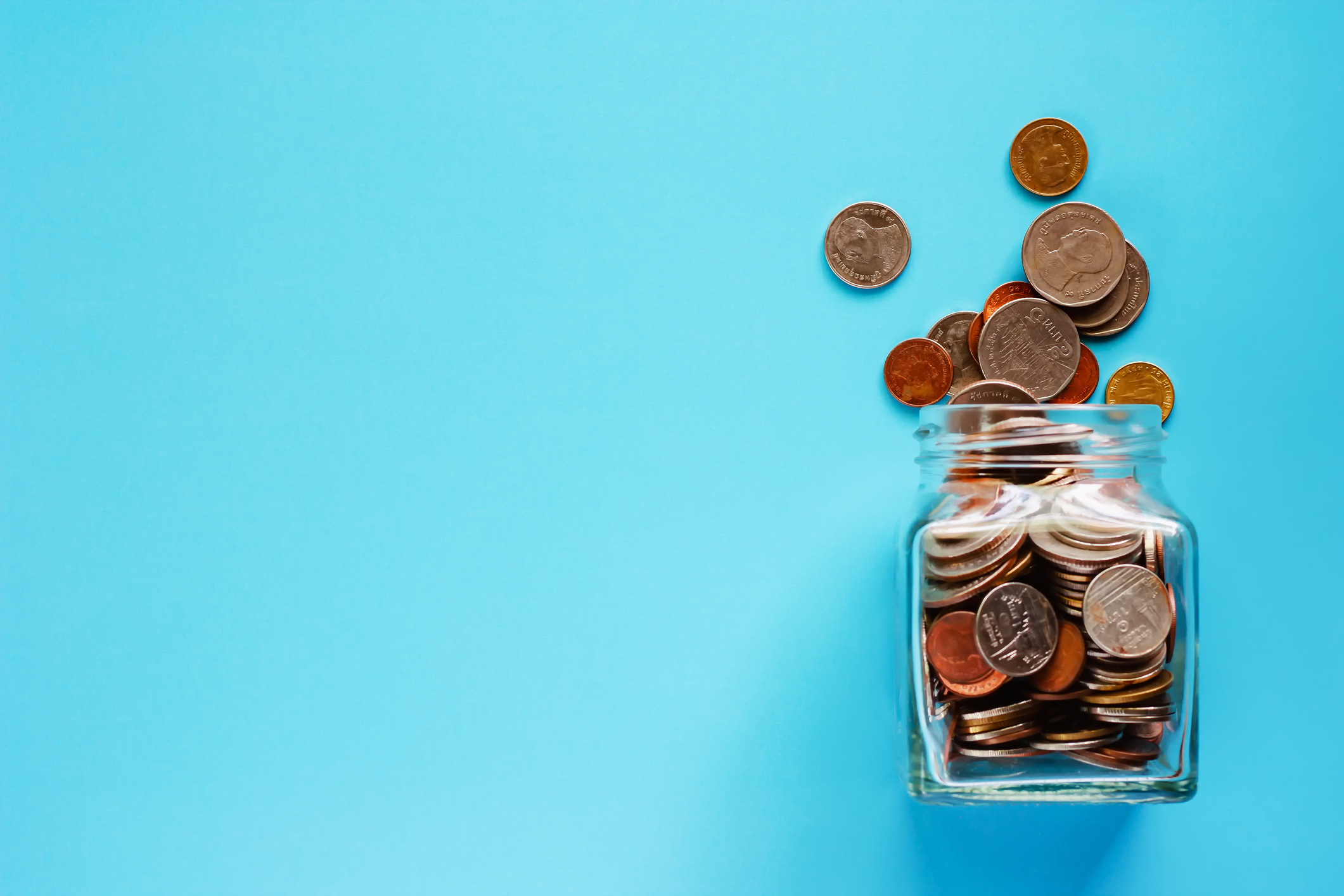 Coins in glass jar and outside, Thai currency money on blue background for business and finance concept