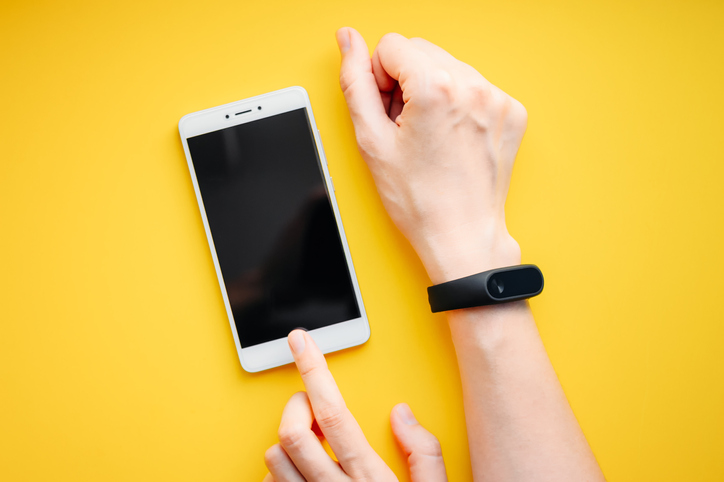 Woman hand with fitness tracker and smartphone on a yellow background