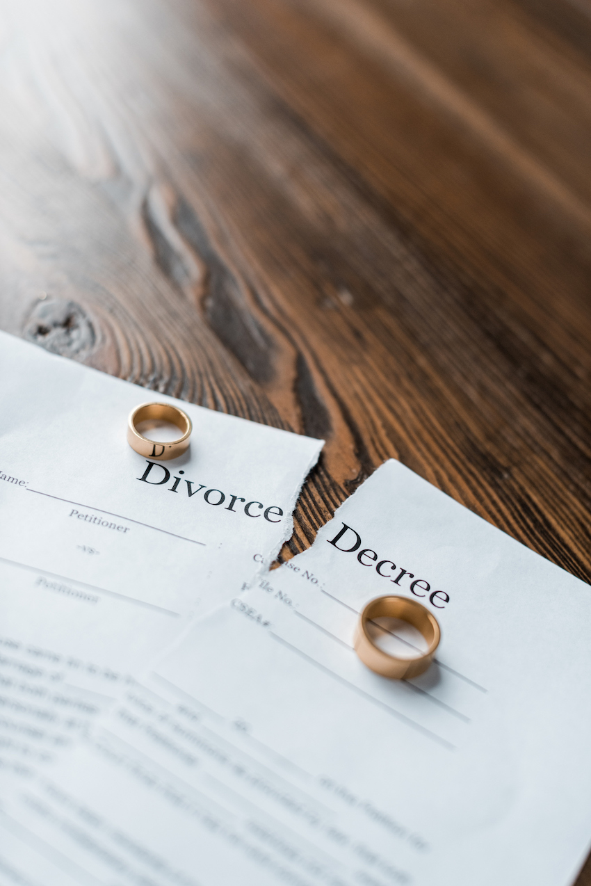 close-up shot of teared divorce decree and engagement rings on wooden tabletop