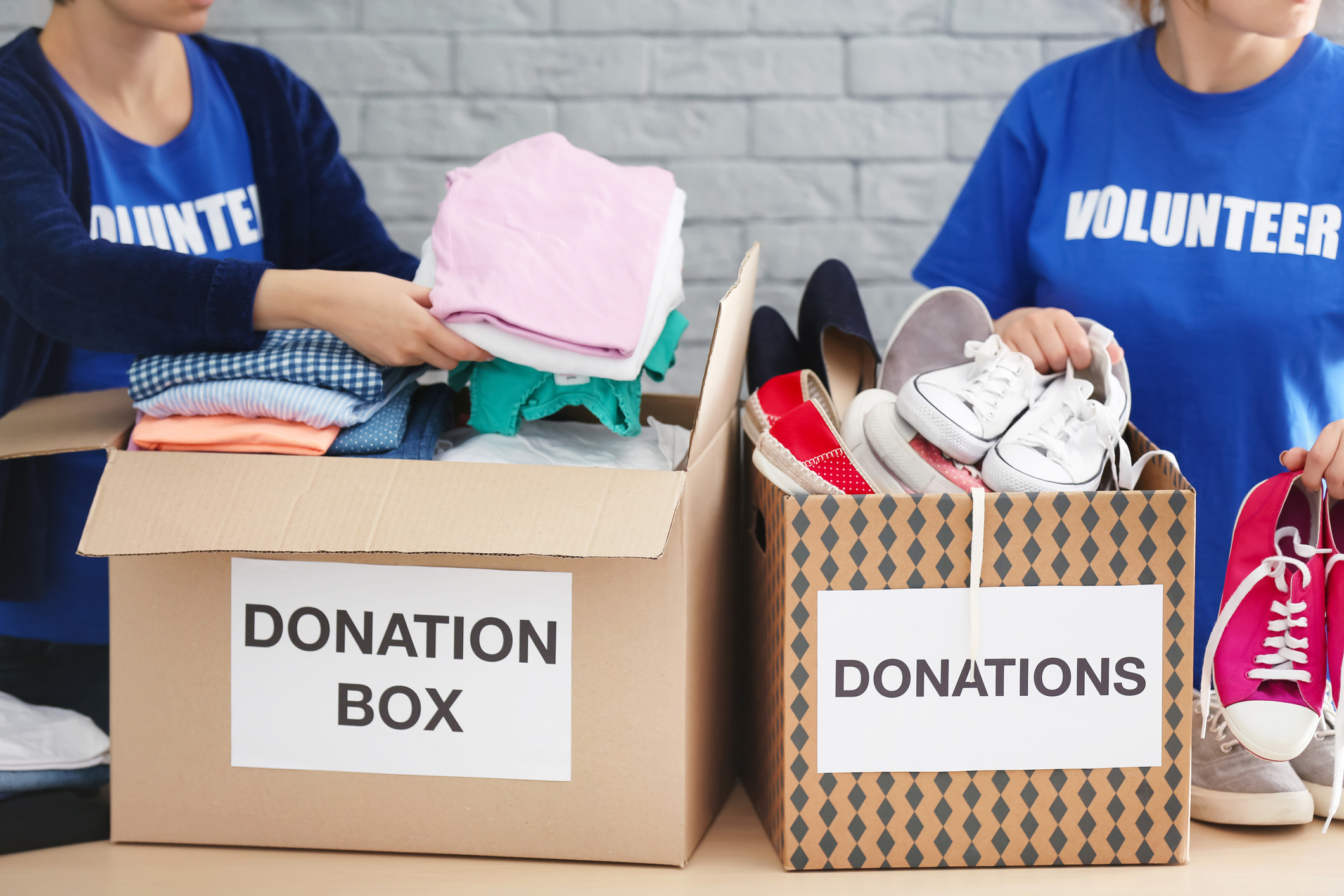 Female volunteers collecting clothes and shoes into donation boxes indoors