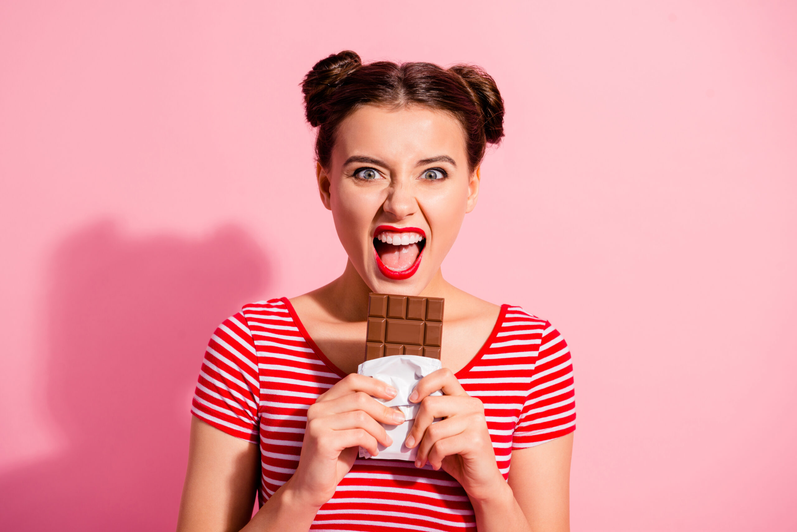 Close-up portrait of her she nice cute charming crazy attractive lovely comic childish girl wearing striped t-shirt biting favorite desirable dessert isolated over pink pastel background