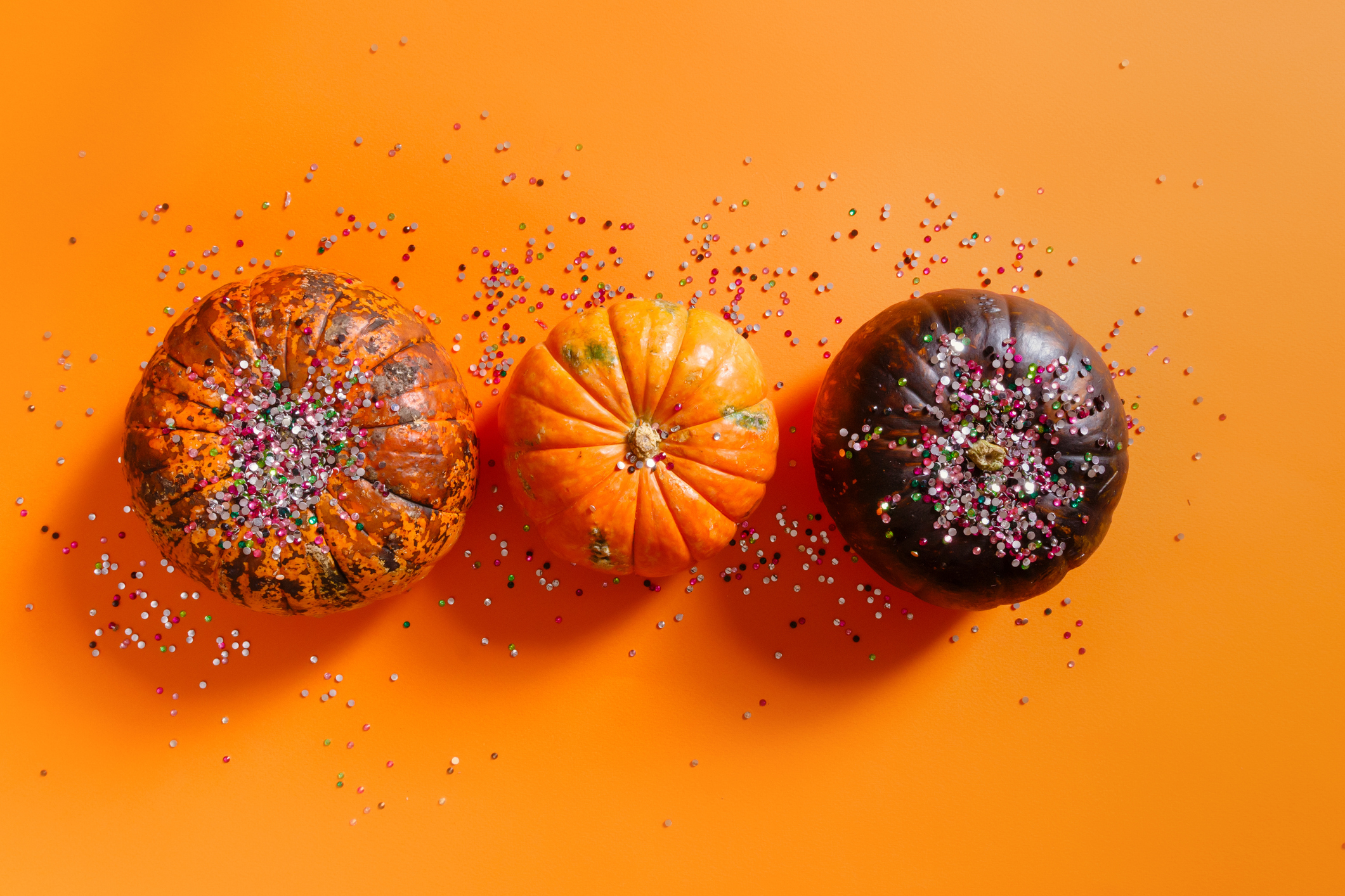 Decorative pumpkins and glitter, festive Halloween composition on a orange background.Flat lay