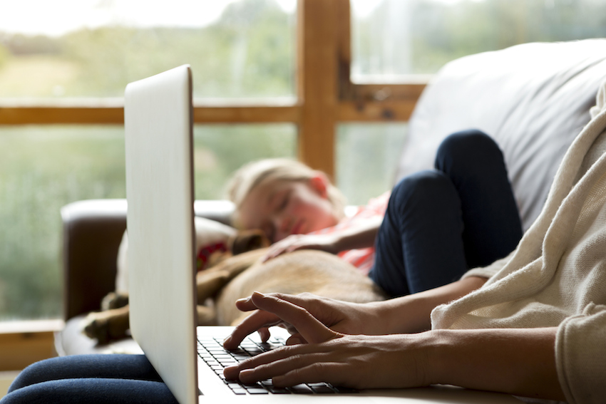 Mother using laptop whilst daughter sleeps