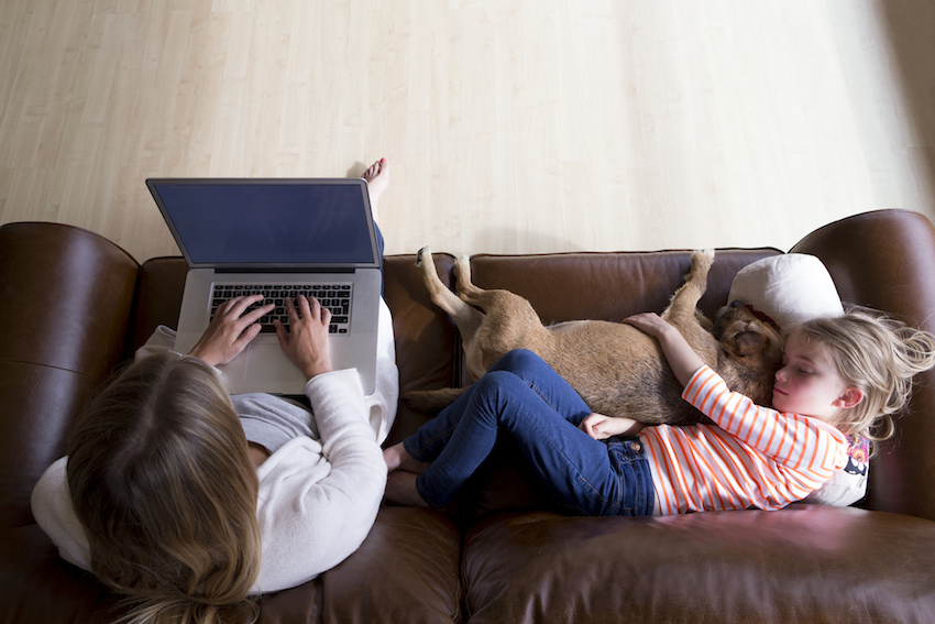 woman using laptop while daughter and dog sleep