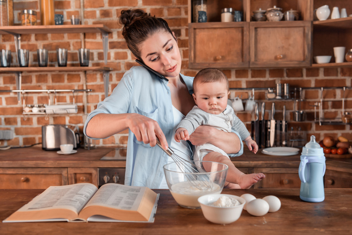 mother holding her son, talking on smartphone and mixing a dough