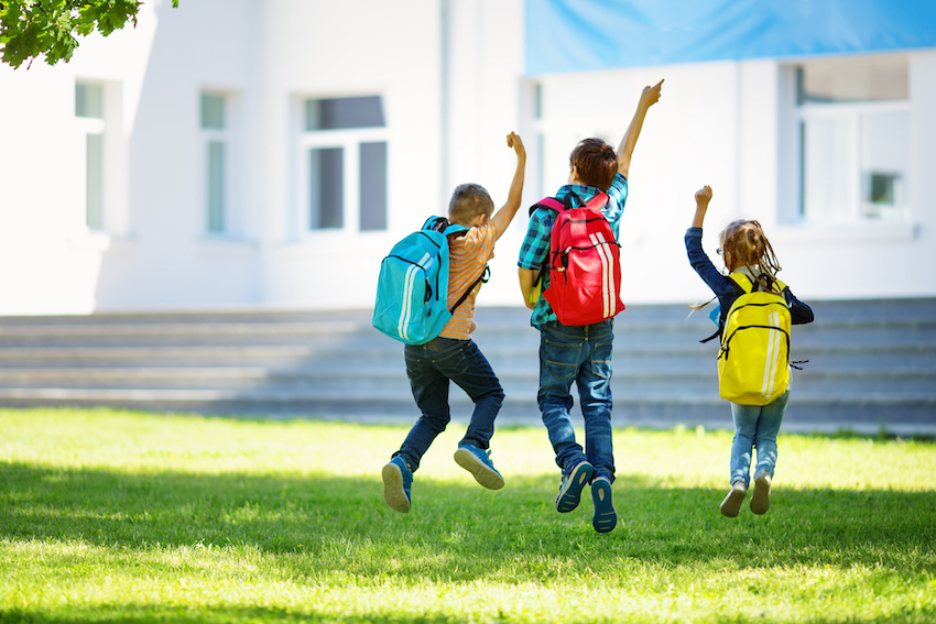 Children with rucksacks jumping in the park near school