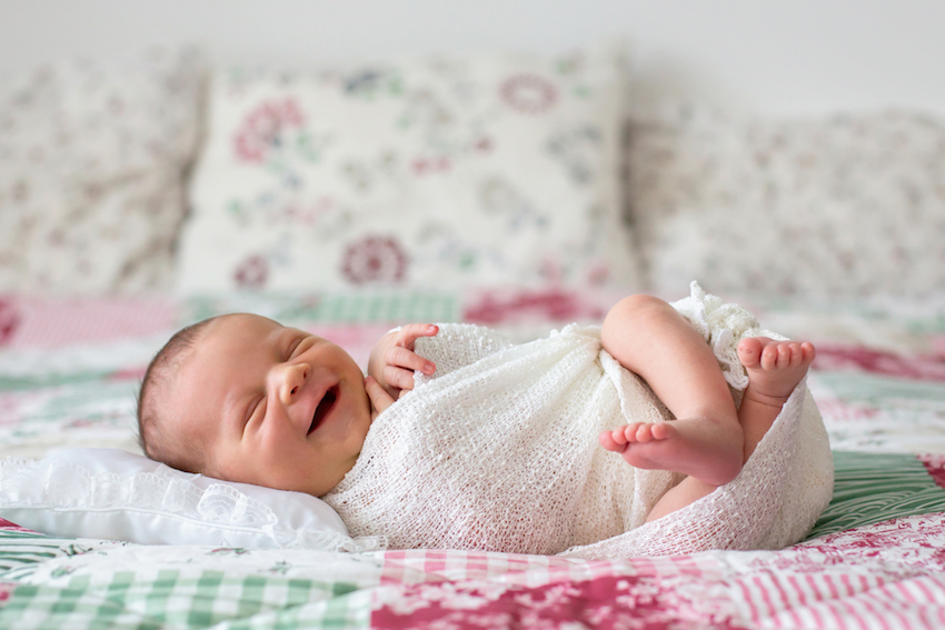 Beautiful newborn baby boy, widely smiling, wrapped in wrap, lying down in bed