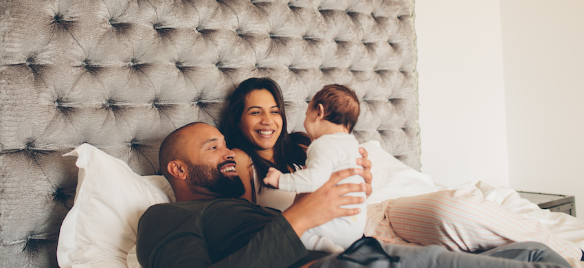 Happy parents playing with their newborn son on bed