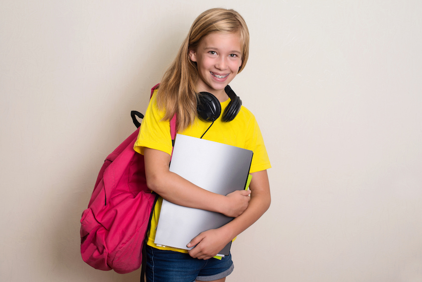 Teen girl student in yellow t-shirt with backpack and headphones smiling. Education.
