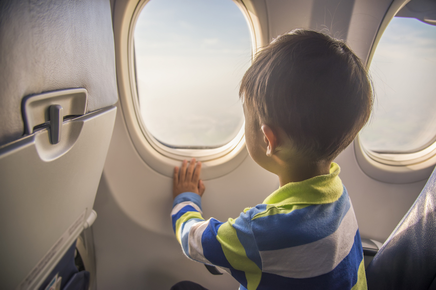 asian boy looking aerial view of sky and cloud outside airplane window while sitting on airplane seat.