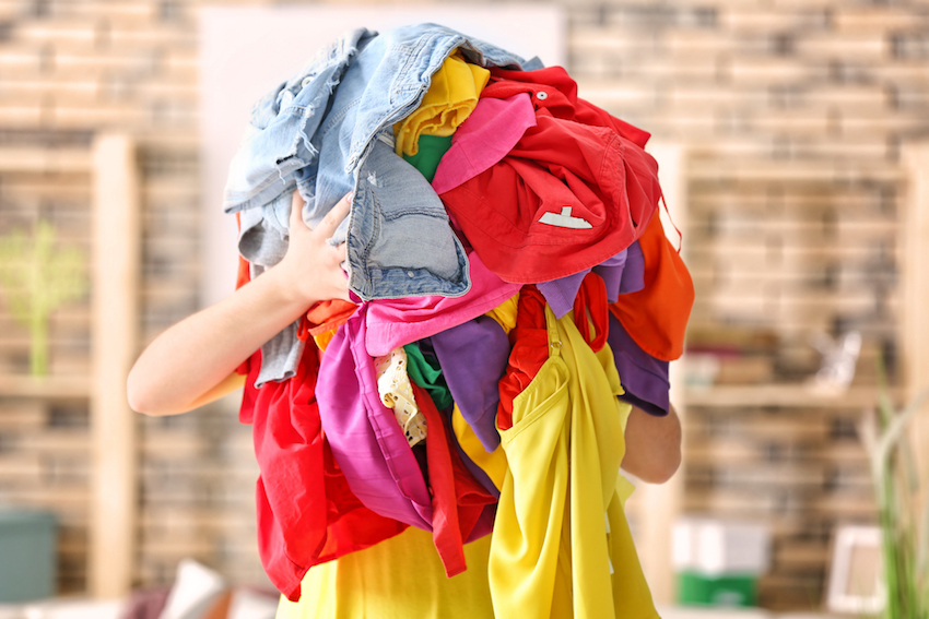 Woman holding pile of colorful clothes indoors