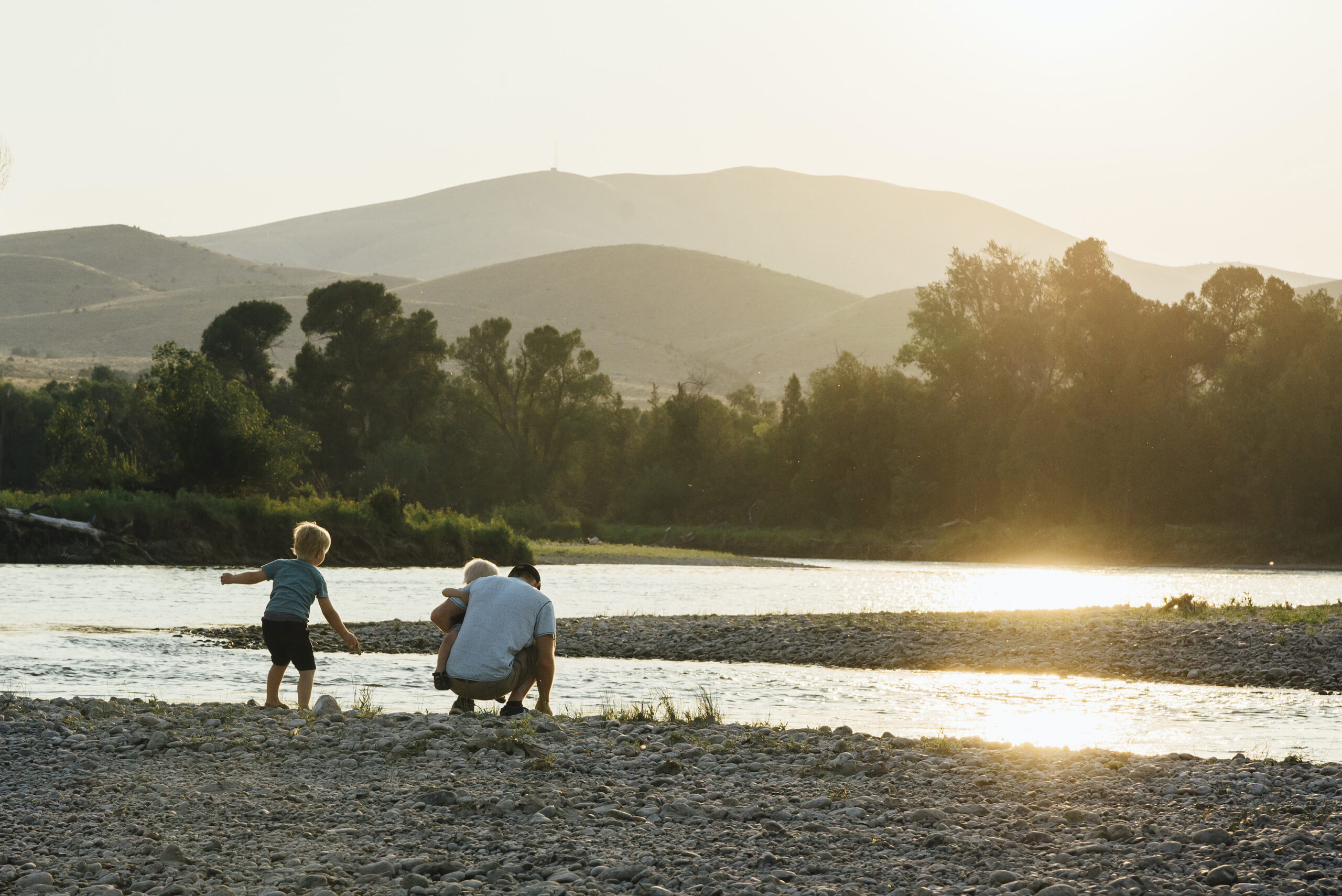 Rear view of father with sons playing at lakeshore against clear sky during sunset