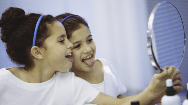 Side profile of two girls looking in a mirror making faces