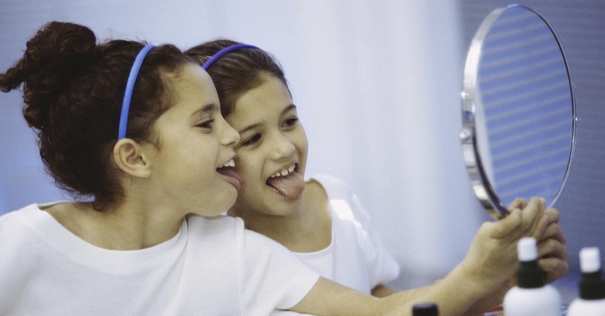 Side profile of two girls looking in a mirror making faces