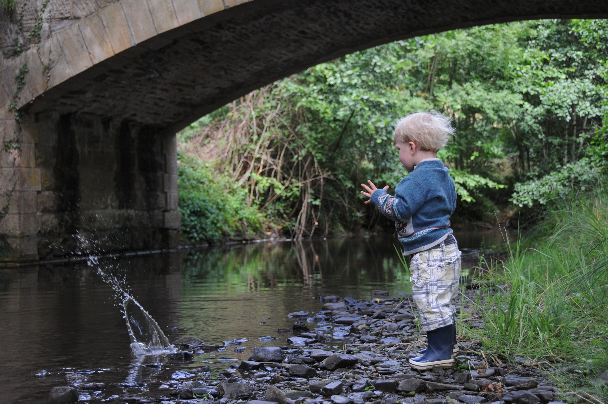 Young toddler throwing rocks into a stream.