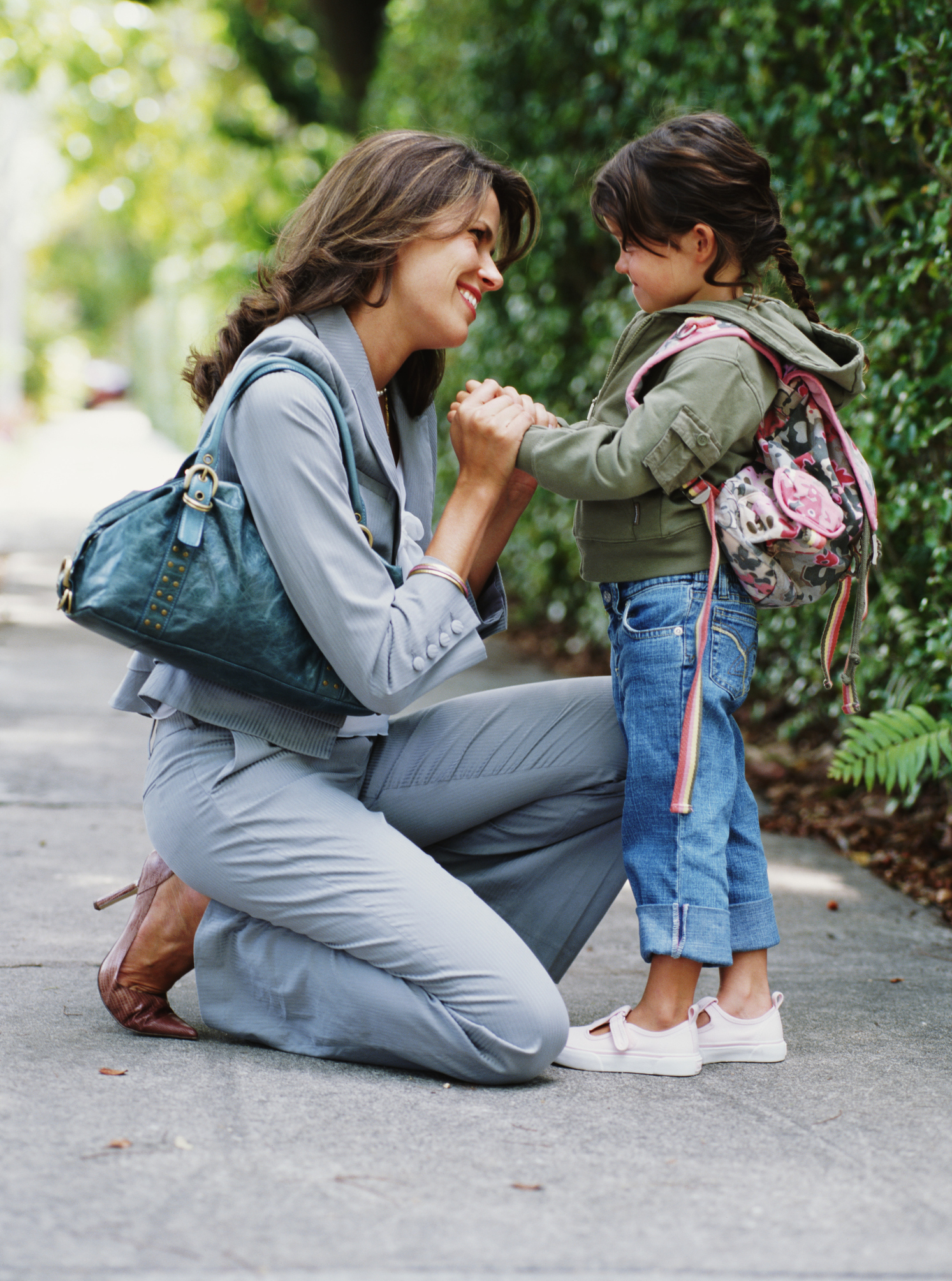 Mother kneeling on pavement, holding hands of daughter (4-6 years), smiling, side view