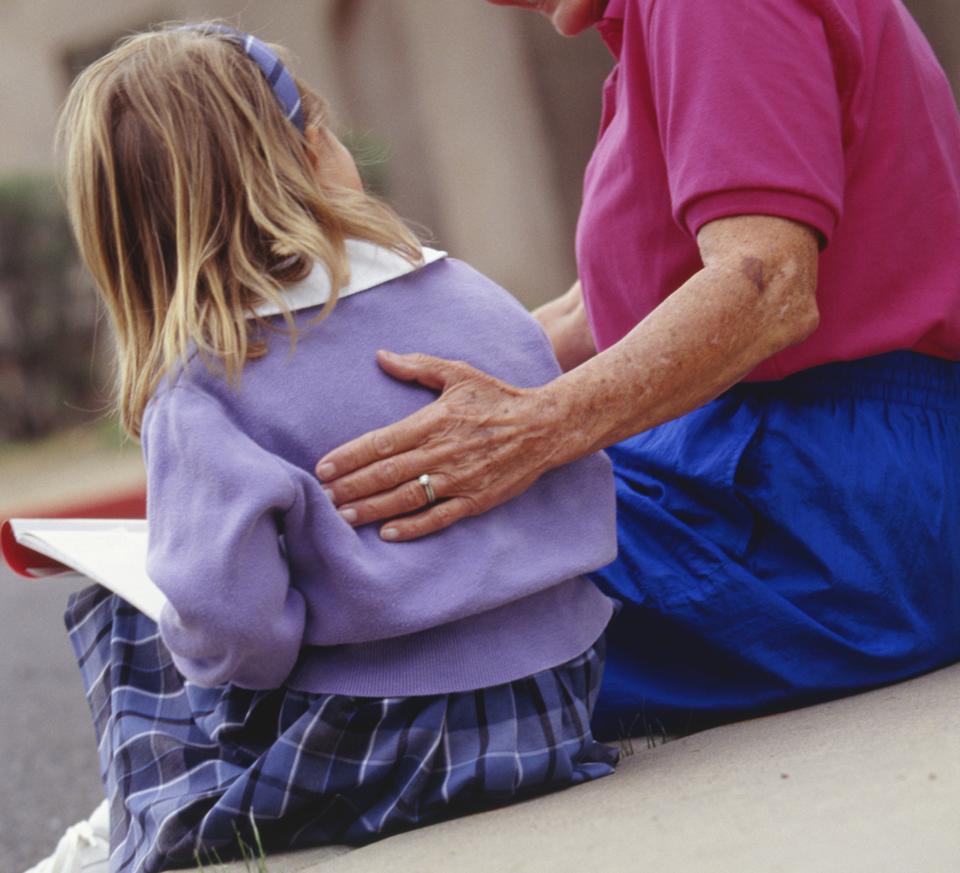 Grandmother and granddaughter sitting outdoors, rear view