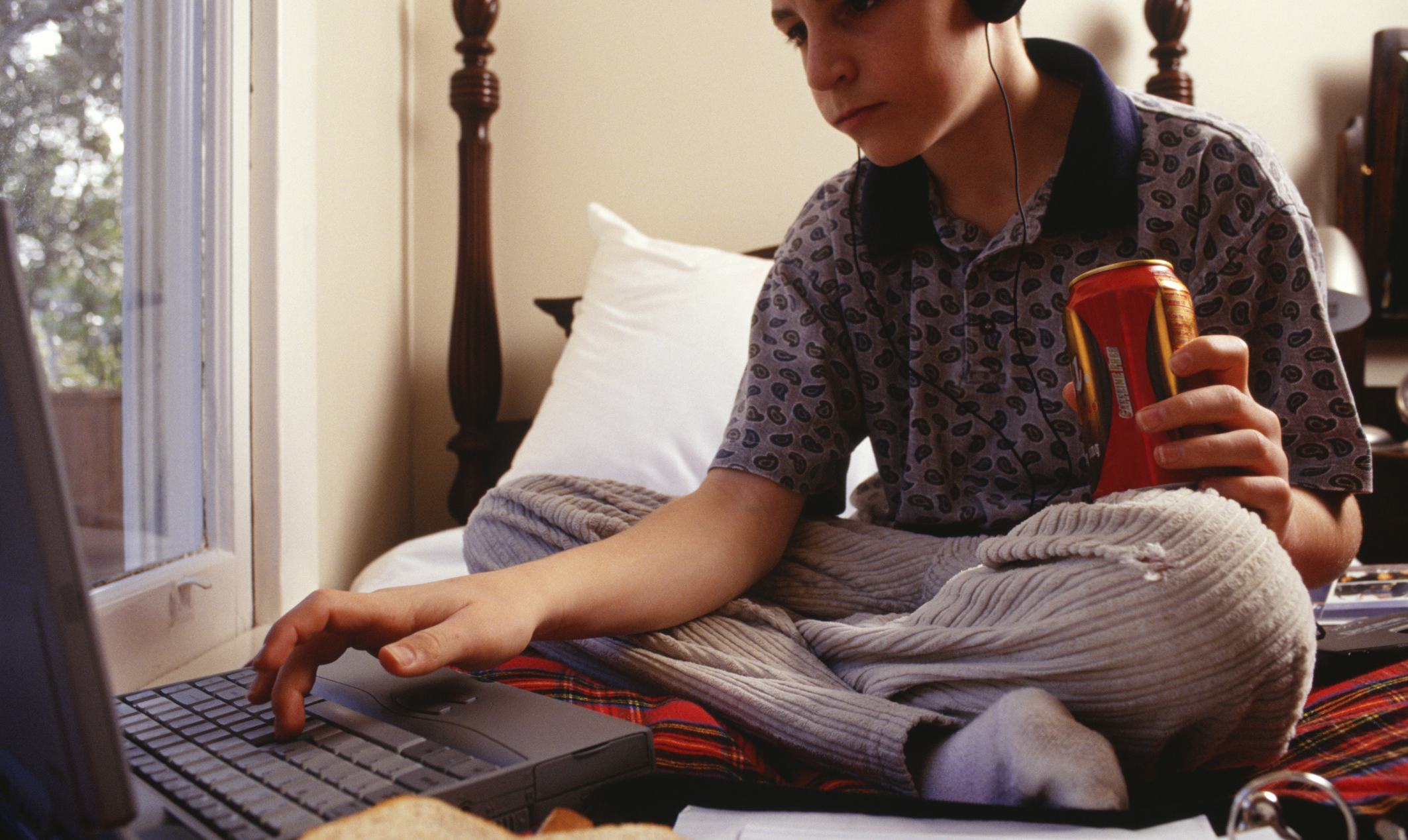 Teenage boy (16-17) using laptop, sitting on bed