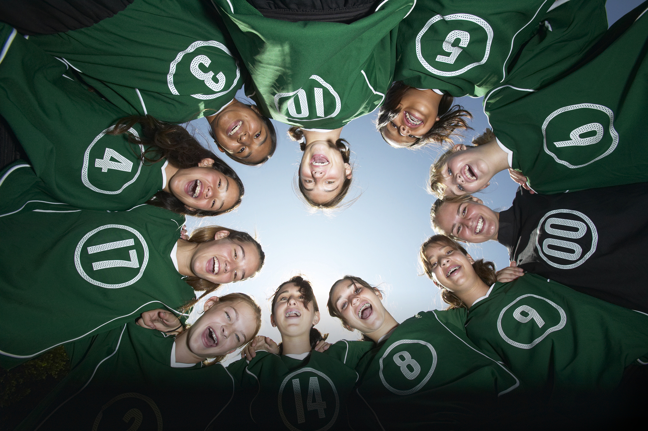 Girls (12-15) football team forming huddle, view from below