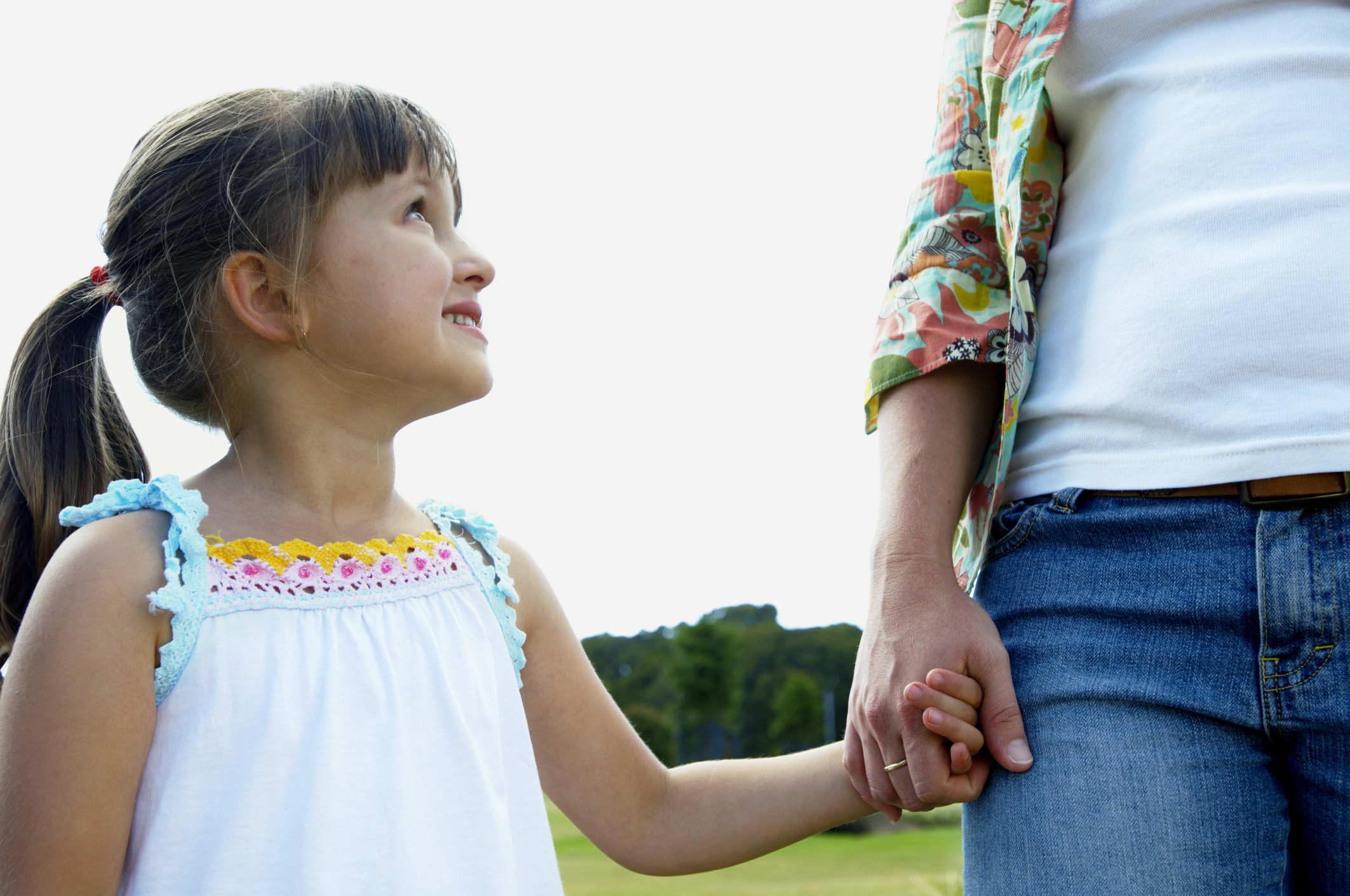 Woman holding daughter's (3-5) hand in park, girl smiling up at mother