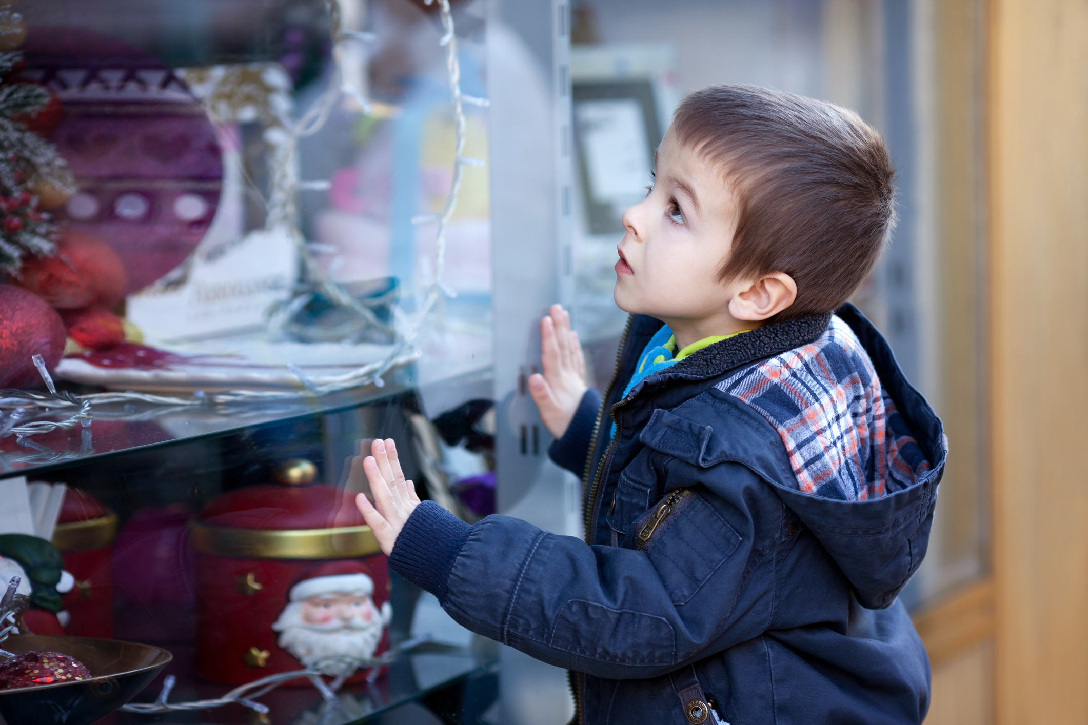 Sweet little boy, looking through a window in shop