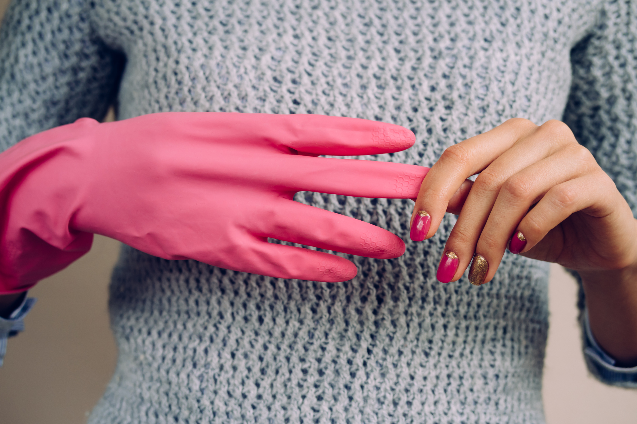 Woman in a gray sweater removes pink cleaning gloves closeup