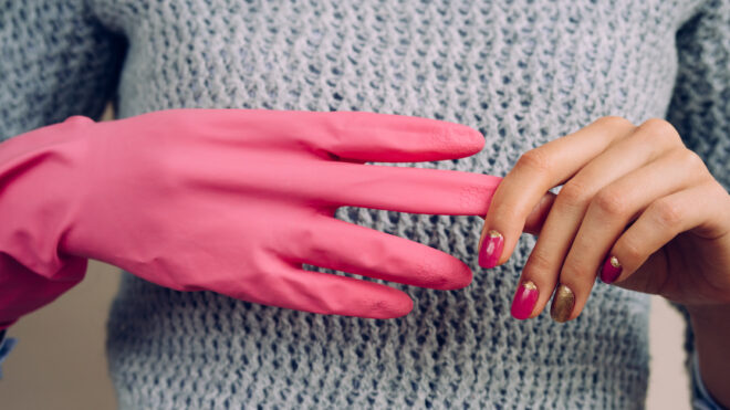 Woman in a gray sweater removes pink cleaning gloves closeup