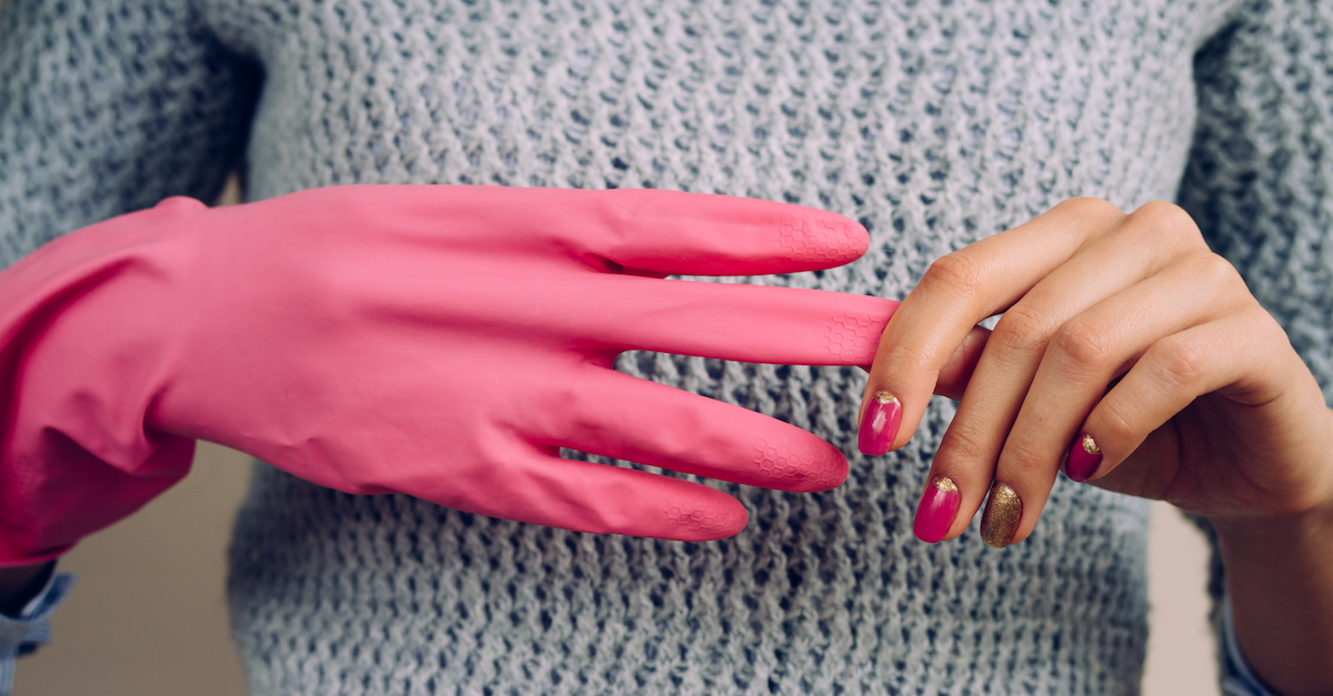 Woman in a gray sweater removes pink cleaning gloves closeup