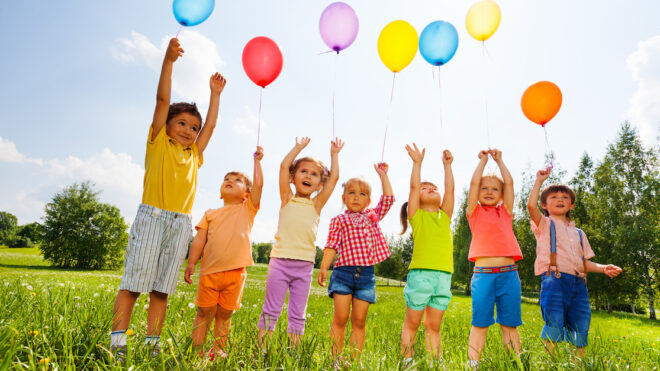 Happy kids with balloons and arms up in the sky