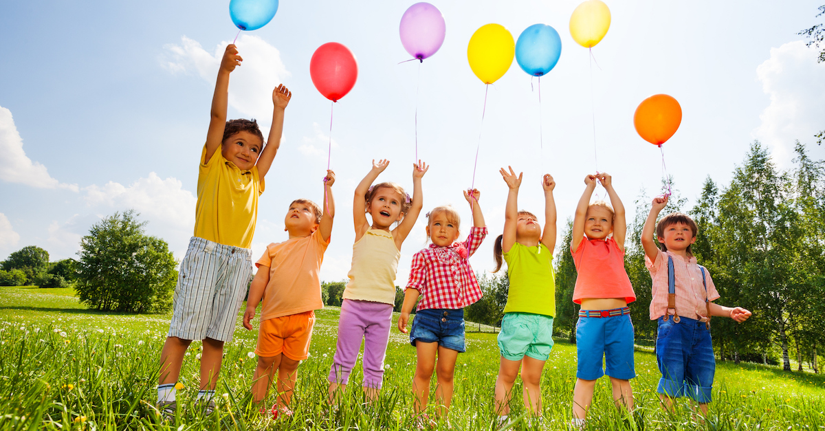 Happy kids with balloons and arms up in the sky