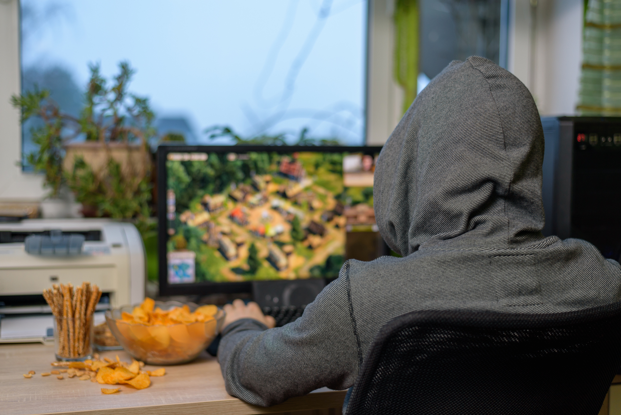 male gamer playing strategy game on computer eating snacks