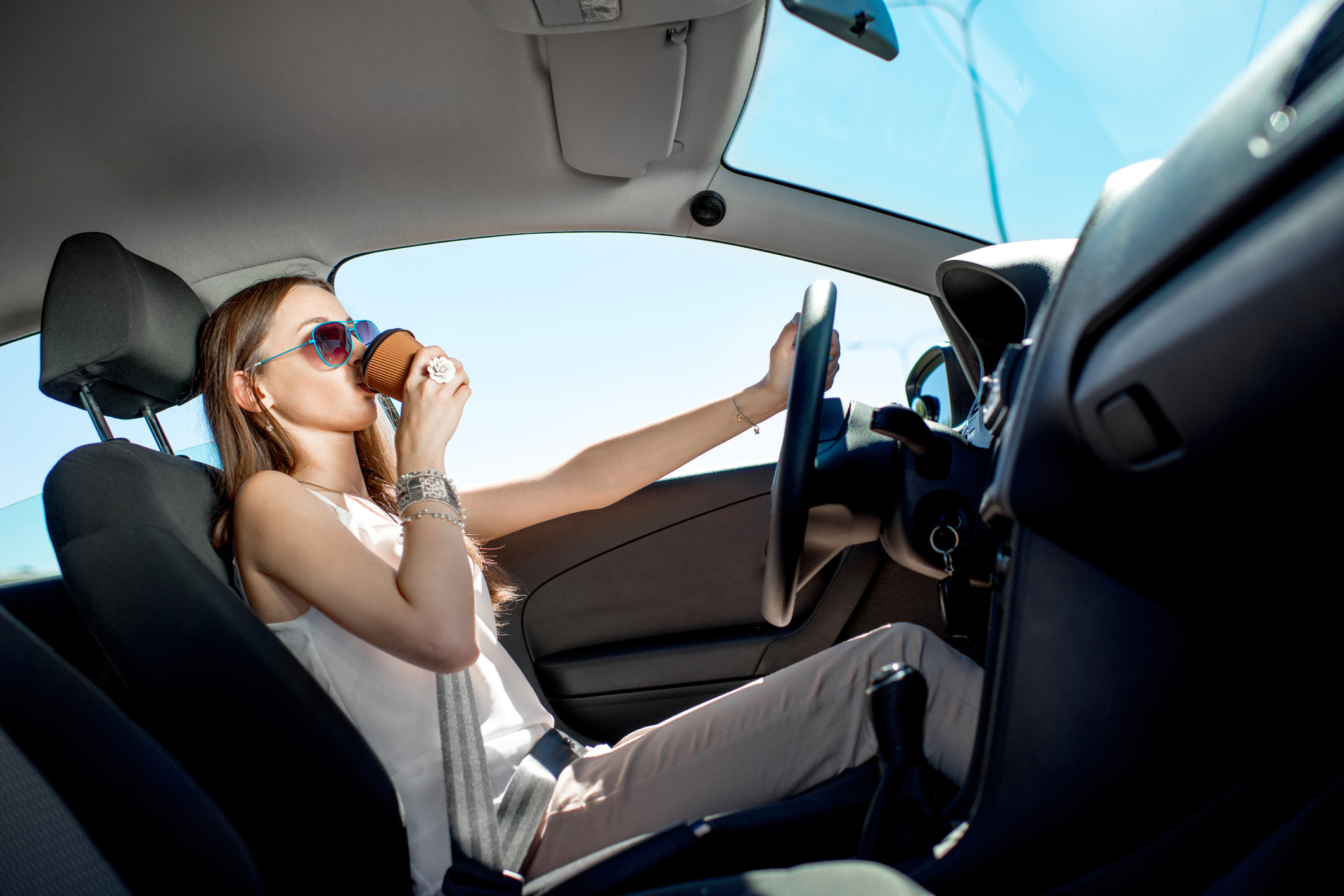 Happy young woman with coffee to go driving her car