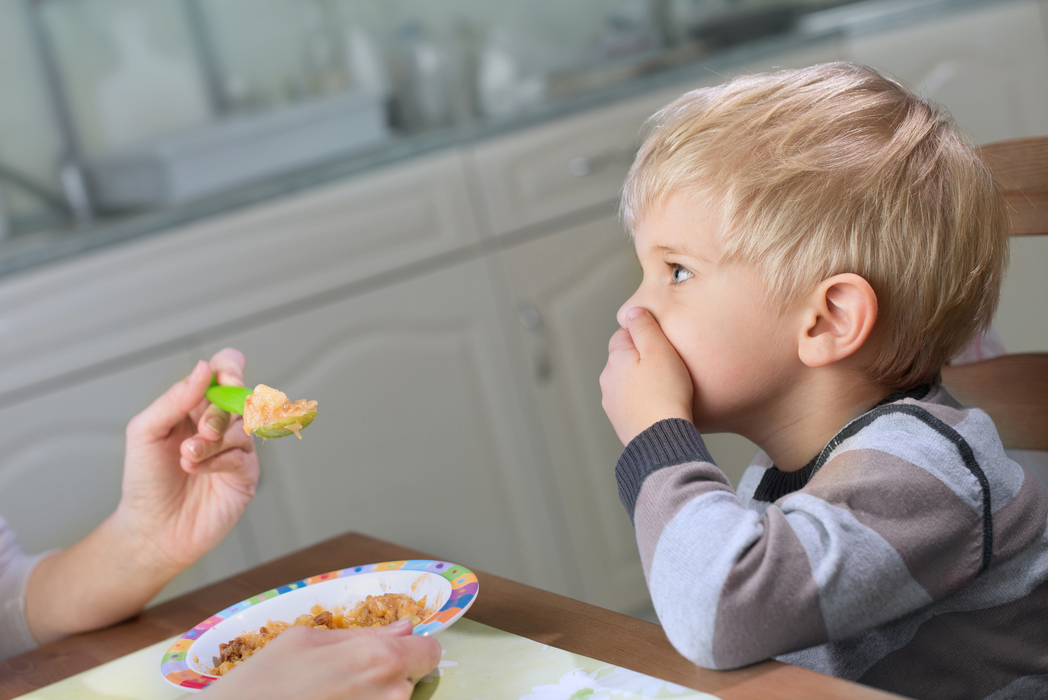 Blond boy holds hand on his mouth to stop eating