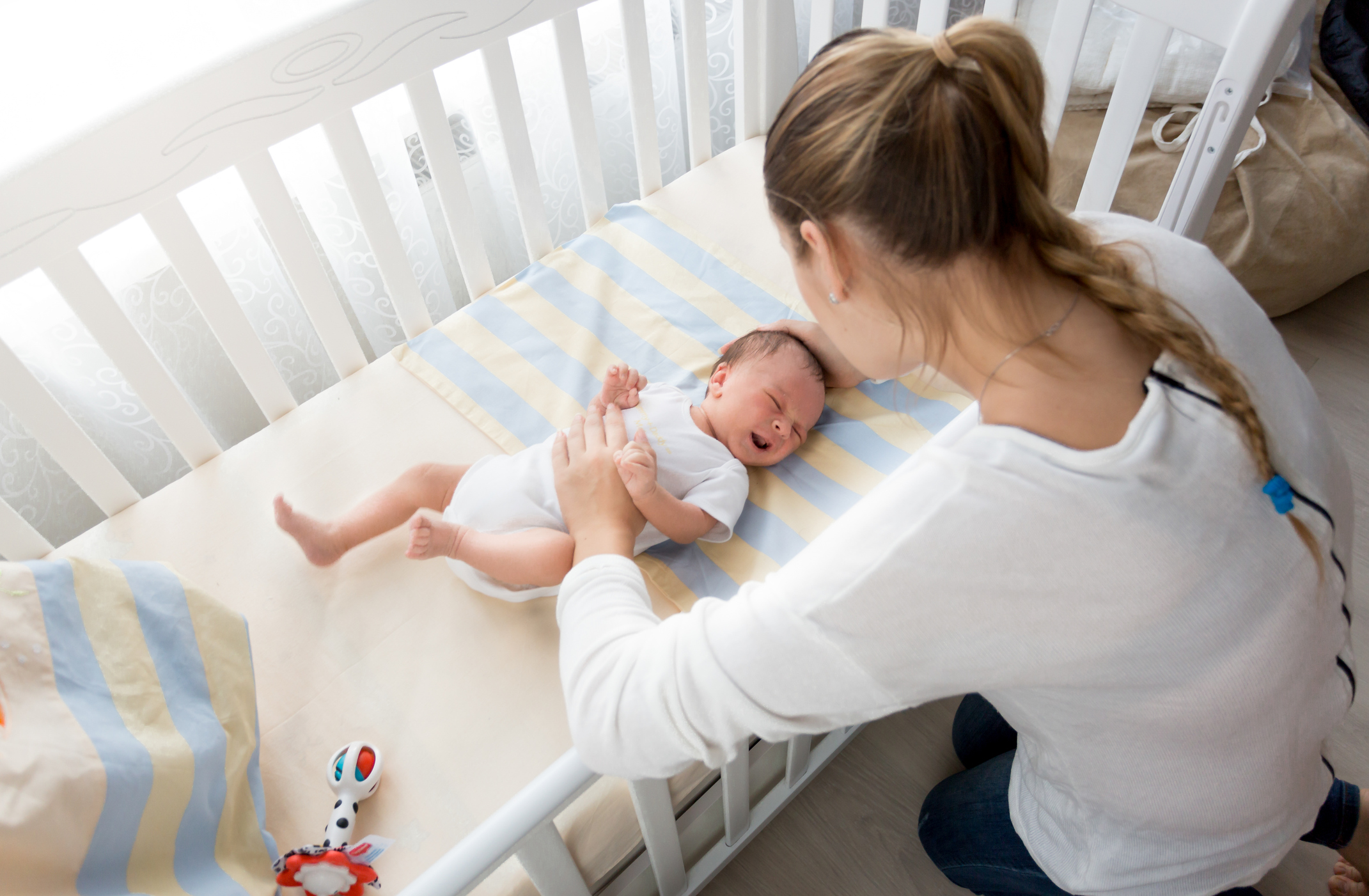 Mother sitting near the cradle and holding baby's hand