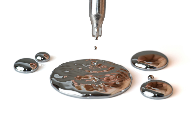 Drops of mercury fall from a pipette, isolated on white.