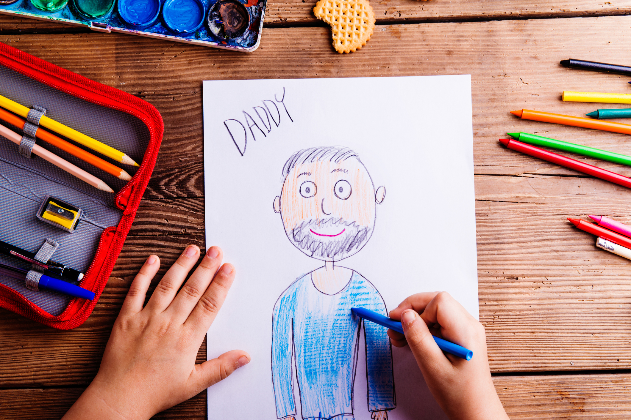 Unrecognizable girl drawing picture of her father. Wooden backgr