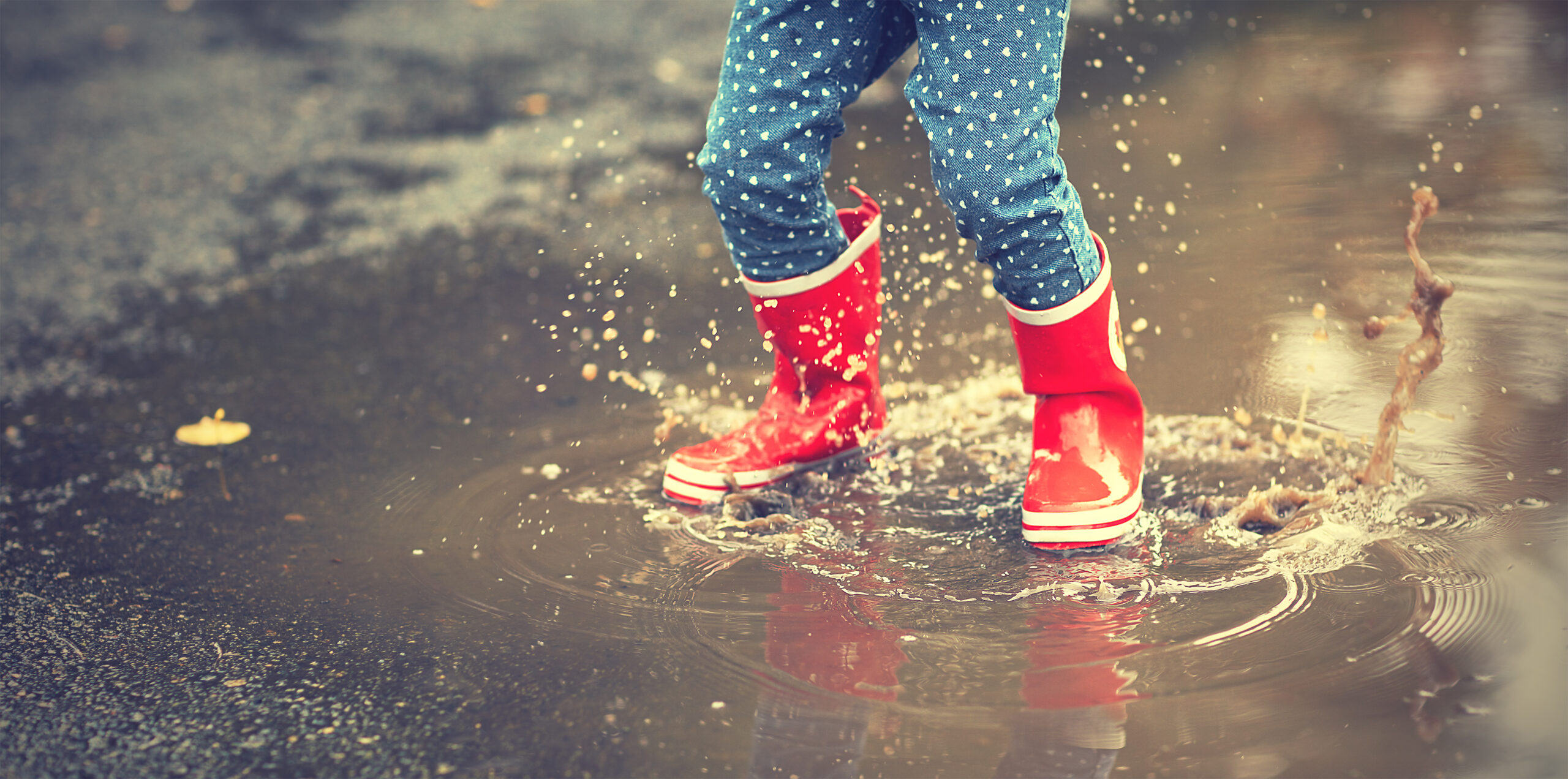 legs of child in red rubber boots jumping in puddles