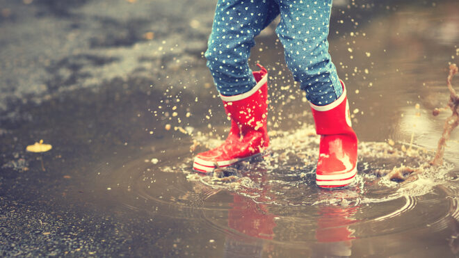 legs of child in red rubber boots jumping in puddles