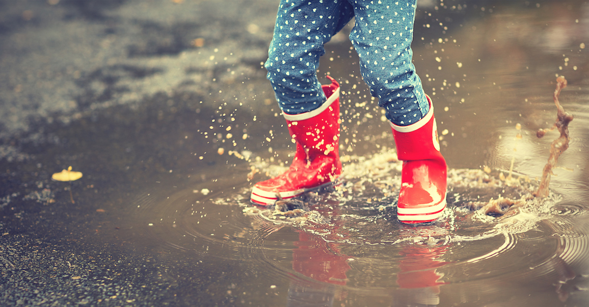 legs of child in red rubber boots jumping in puddles