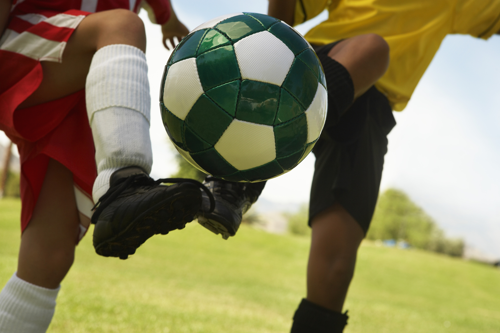 Two little league players (7-9 years) kicking ball mid air, mid section, close up