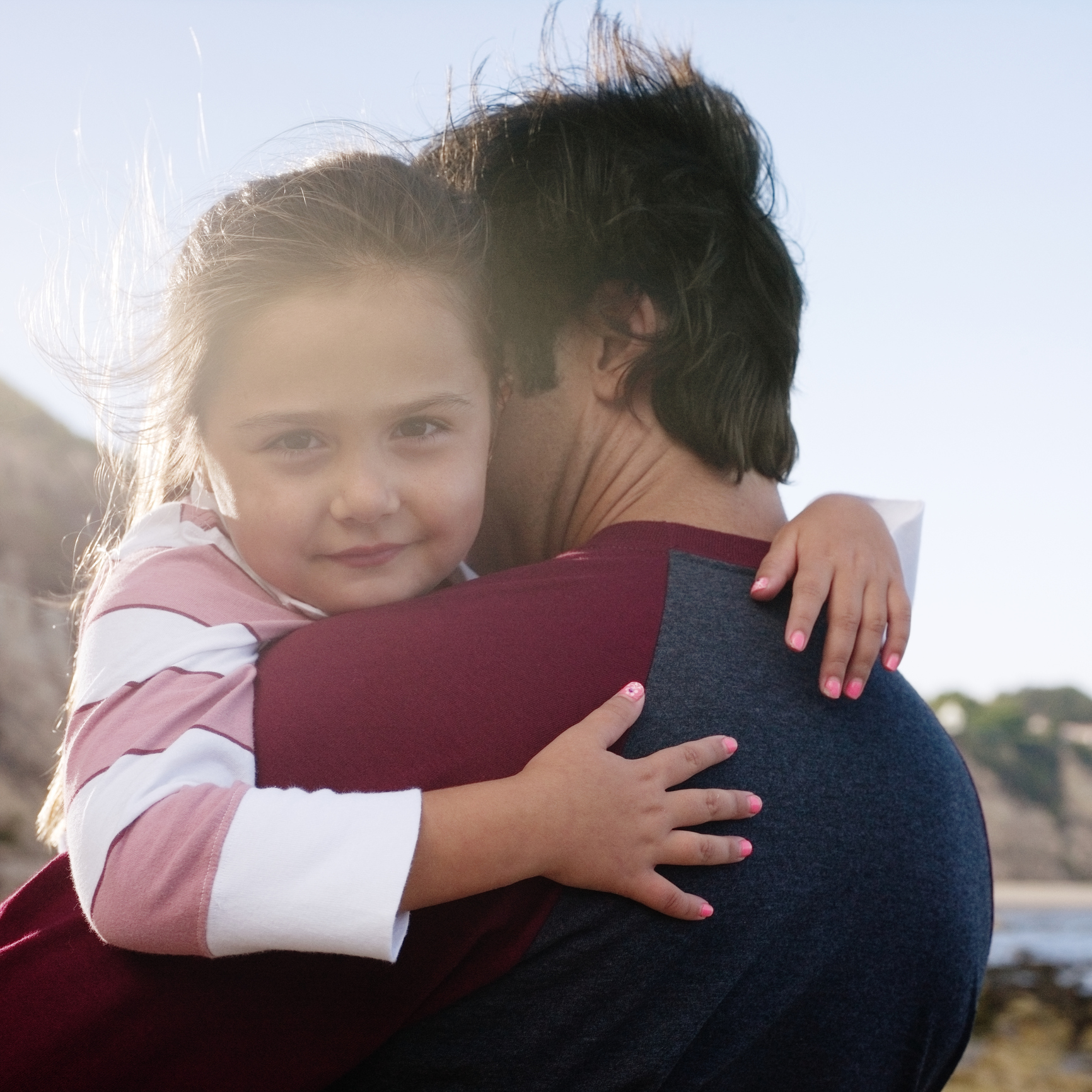 Daughter (6-7) and father hugging, girl looking at camera, outdoors