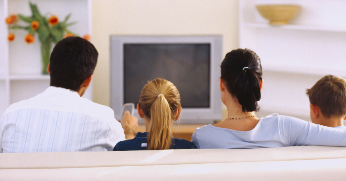 Rear view of a couple sitting on the couch in front of a television with their children (8-10)