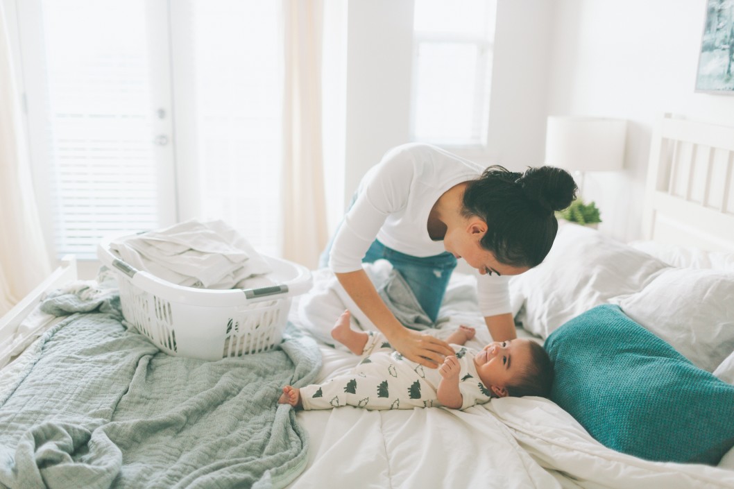 a-mother-playing-with-her-baby-while-doing-laundry-in-a-bright-clean-bedroom_t20_2wm2mZ.jpg