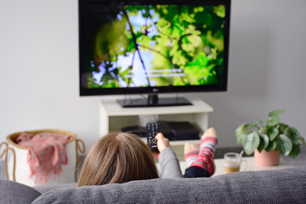 a-young-woman-from-behind-watching-tv-and-changing-channels-with-tv-remote-control-while-sitting-on_t20_RzK1om.jpg