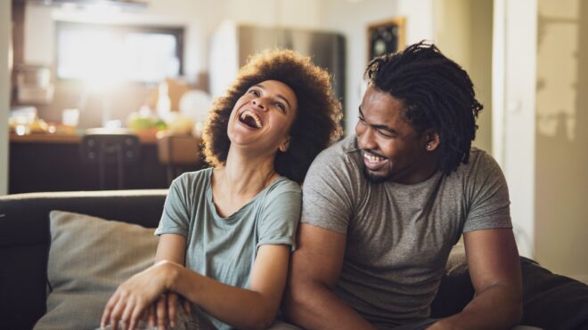 Cheerful black couple having fun while relaxing on sofa at home.