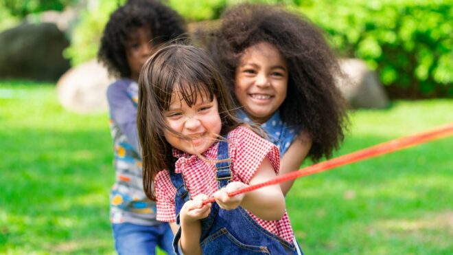 Happy children playing tug of war in the park.